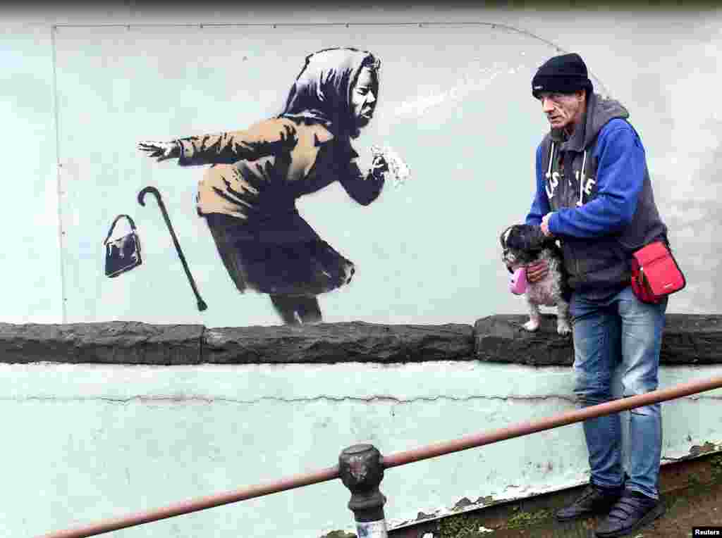 A man stands near a new street artwork entitled "Aachoo!!" by Banksy in Totterdown, Bristol, Britain.