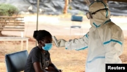 FILE - A woman has her temperature checked by a health care worker during a nationwide lockdown to help curb the spread of the coronavirus, at a screening center in Harare, Zimbabwe, April 30, 2020.