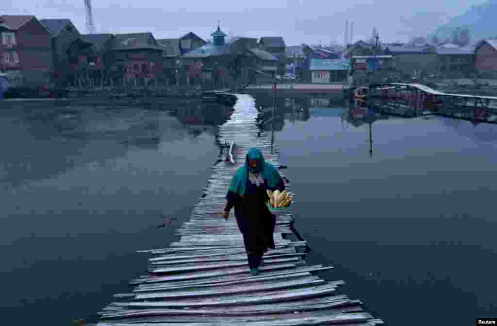 A woman carries bread as she walks on a frost-covered footbridge of the Nigeen Lake on a cold winter morning in Srinagar, India.