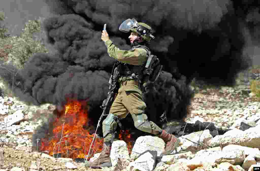 A member of the Israeli security forces takes a photograph with his telephone during clashes with Palestinian protesters after a weekly demonstration in the West Bank village of Kfar Qaddum.