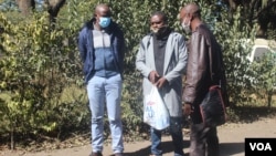 Journalists Samuel Takawira and Frank Chikowore stand with a police detective outside a court in Harare, Zimbabwe, May 23, 2020. (Columbus Mavhunga/VOA) 