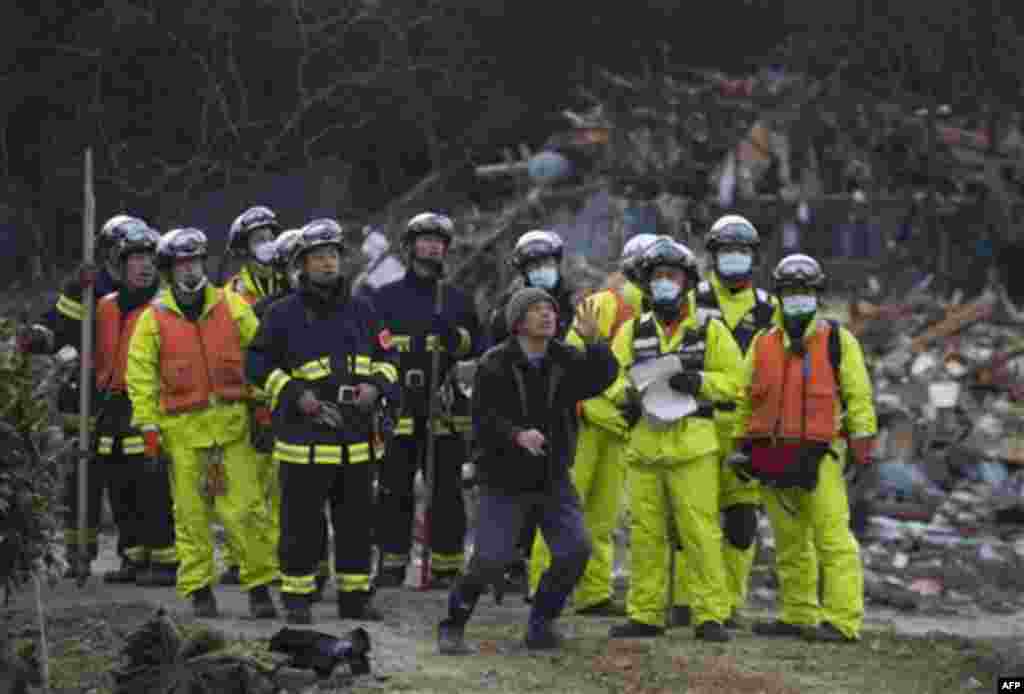 A survivor of the tsunami that swept through his village of Saito, in northeastern Japan, retells the story to a rescue team that arrived to search the area Monday, March 14, 2011. Rescue workers used chain saws and hand picks Monday to dig out bodies in