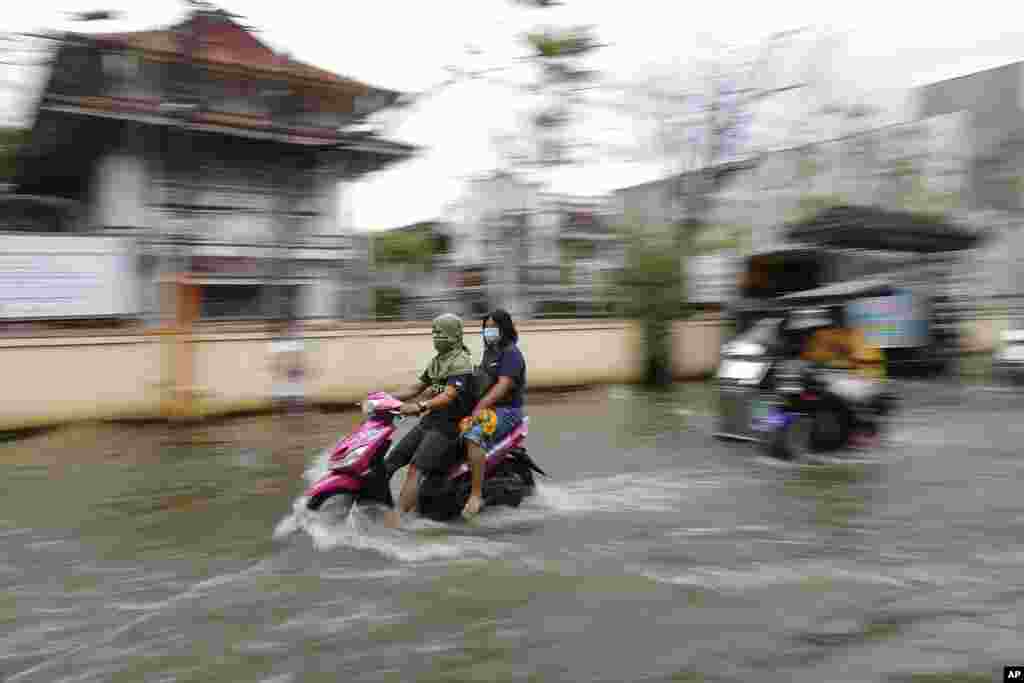 Residents wear masks to prevent the spread of the coronavirus ride motorcycles as they negotiate a flooded road due to Typhoon Molave in Pampanga province, northern Philippines.