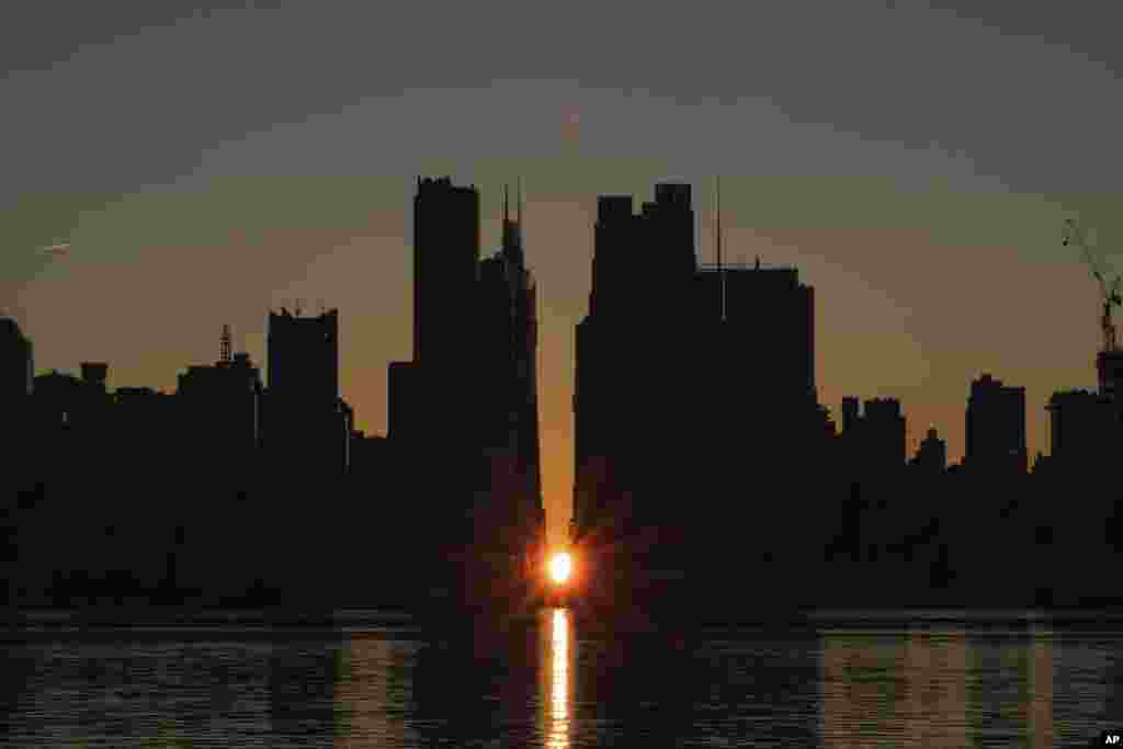 The sun rises through the middle of buildings long 42nd street in New York's Manhattan borough during a phenomenon known as Manhattanhenge as viewed from Weehawken, New Jersey.