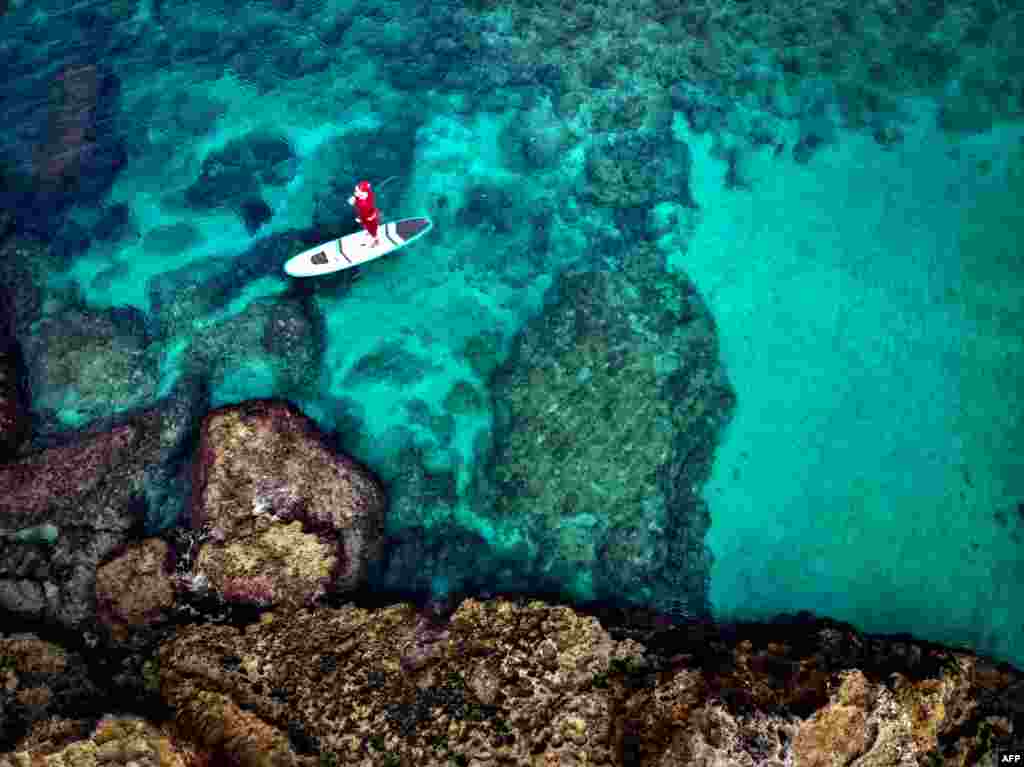 A man dressed with a Santa Claus outfit rides on a standup paddle in Lebanon's northern coastal city of Batroun.