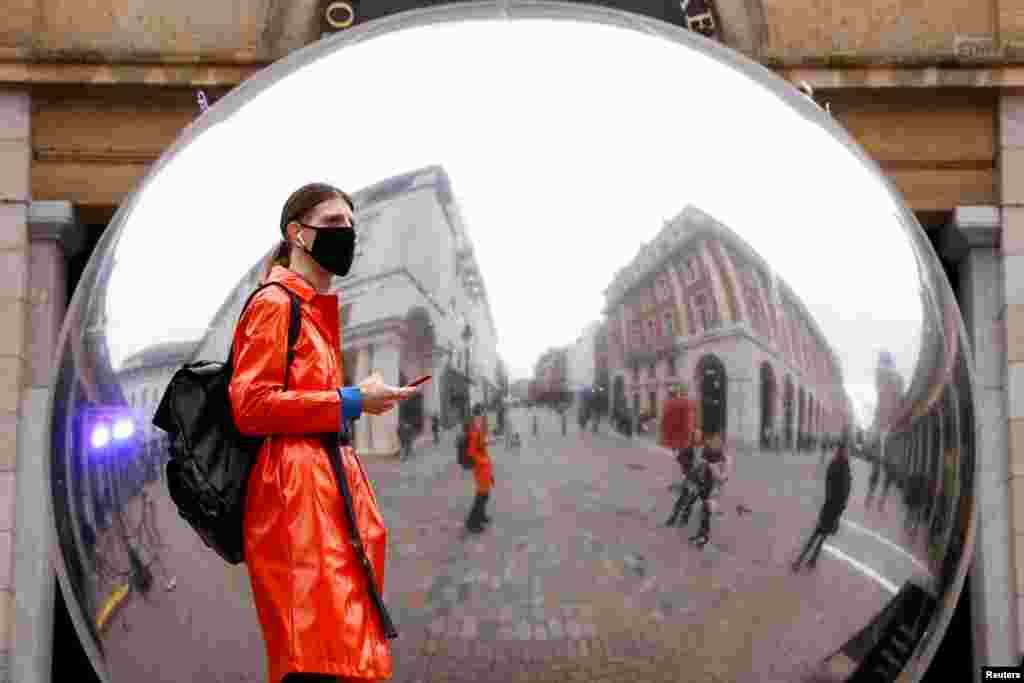 A person wearing a face mask is reflected in an art work entitled "A=V" by Ben Cullen Williams, amid the coronavirus outbreak, in Covent Garden, London, Britain.