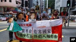 Pro-democracy demonstrators hold up a banner and portraits of jailed Chinese civil rights activists, lawyers and legal activists as they march to the Chinese liaison office in Hong Kong, Thursday, June 25, 2020. The banner read "One-party…