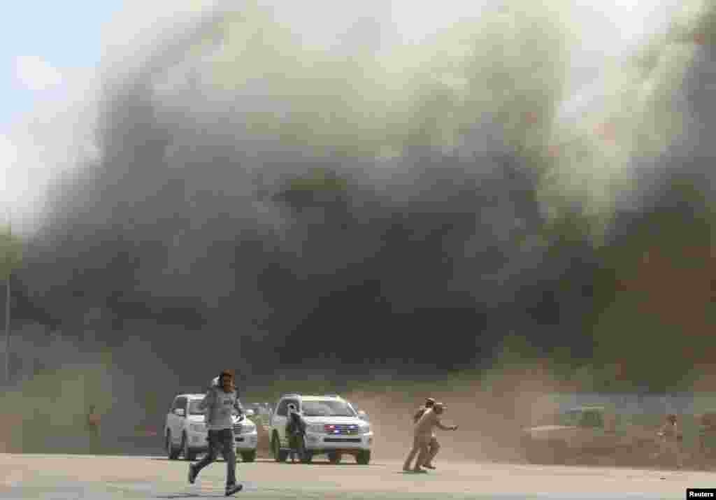 People run as dust rises after explosions hit Aden airport, upon the arrival of the newly-formed Yemeni government in Aden.