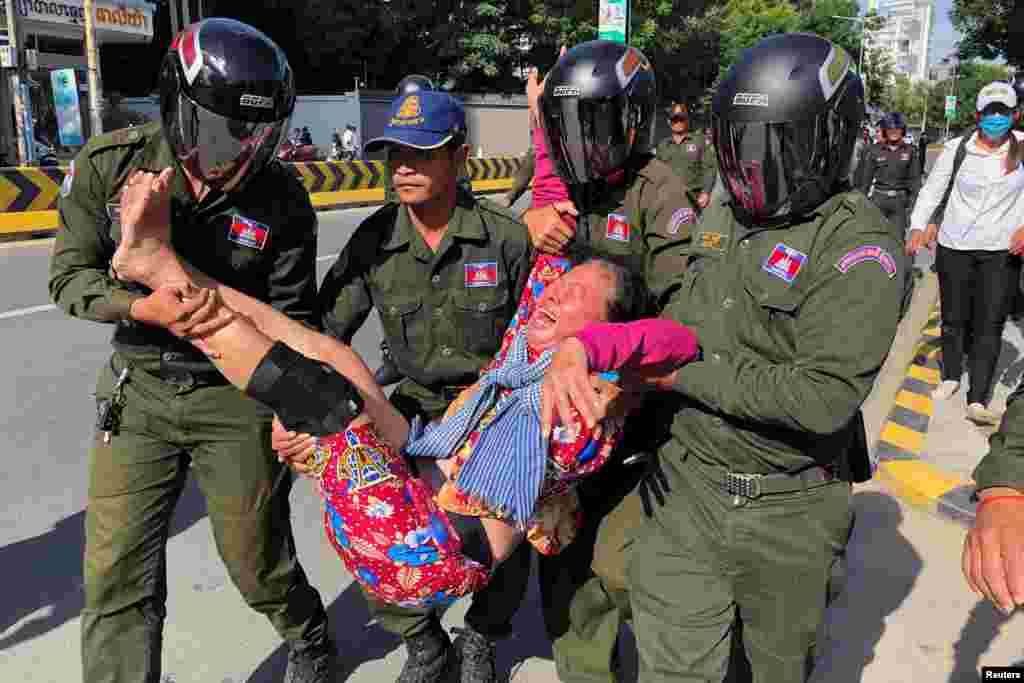 A woman is carried by police officers after security guards broke up a small protest near the Chinese embassy opposing alleged plans to boost Beijing's military presence in the country, in Phnom Penh, Cambodia.