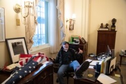 FILE - A supporter of President Donald Trump sits inside the office of Speaker of the House Nancy Pelosi inside the Capitol in Washington, Jan. 6, 2021.
