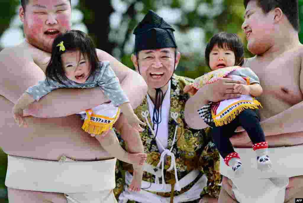 Babies held by student sumo wrestlers cry beside a referee (C) clad in a traditional costume during the "Baby-cry Sumo" competition at Sensoji temple in Tokyo, Japan, April 29, 2013.