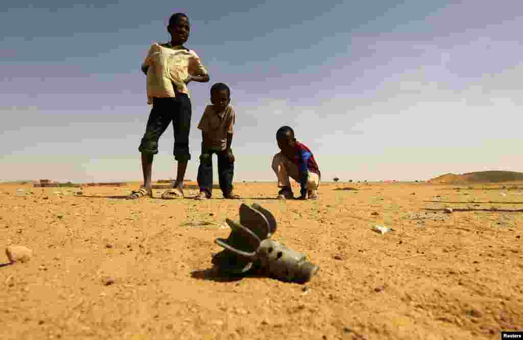 Tiga orang anak laki-laki Sudan mengamati sebuah rongsokan mortir yang ditemukan dekat kamp pengungsi Al-Abassi di Darfur utara, Sudan.