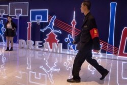 A security guard walks past neon light decor depicting basketball players and silhouette of iconic Chinese buildings in Beijing, Oct. 11, 2019.
