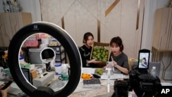 In this May 5, 2020, photo, China's online celebrity Zhang Mofan, right, introduces fresh mangos to her online clients and fans through the live-streaming at her house in Beijing. Retailers in China are embracing livestreaming as a sales channel…