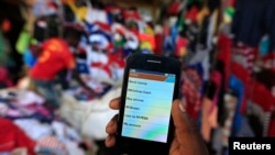 FILE - A man holds up his mobile phone showing an M-Pesa mobile money transaction page at an open-air market in Kibera in Kenya's capital, Nairobi, Dec. 31, 2014.