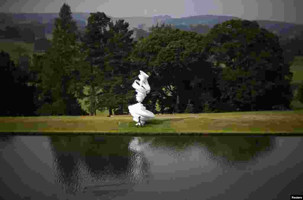 A woman walks past a sculpture by Alice Aycock entitled "Cyclone Twist" during the Beyond Limits selling exhibition at Chatsworth House in central England.