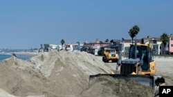 Un tractor apila arena para proteger la playa de la marea que se espera provoque la tormenta Norbert en California.