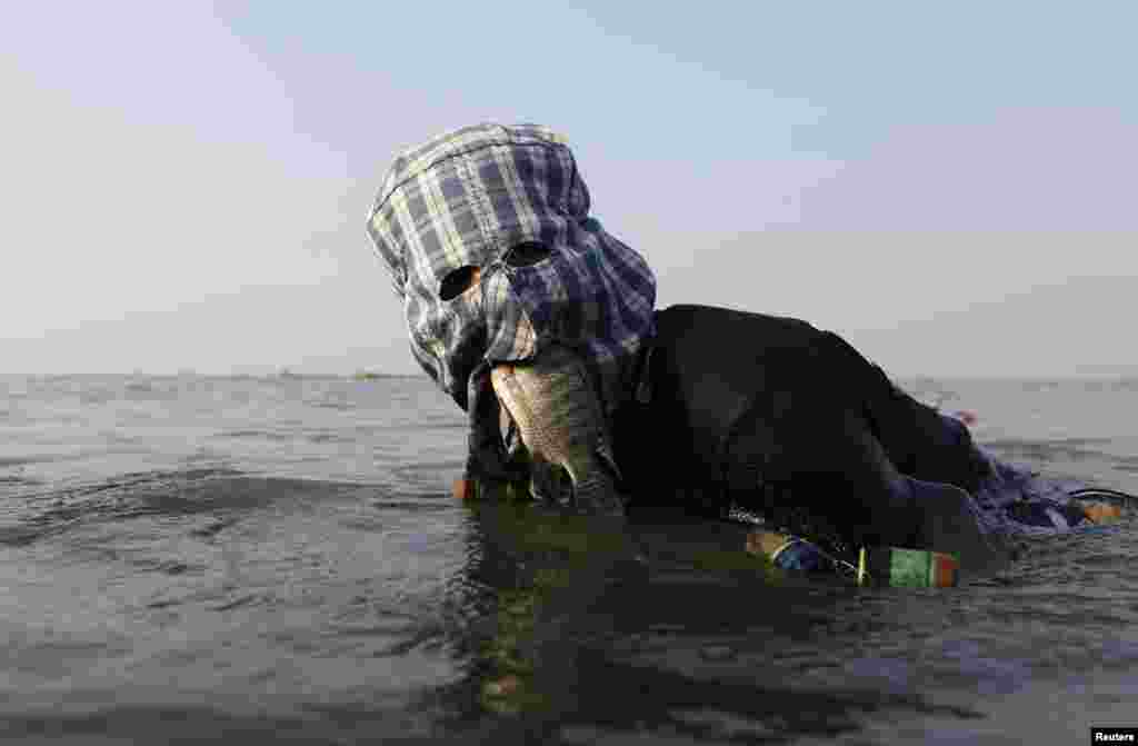 Fisherman Ompong Vargas, 39, who wears a facial mask made of fabric to protect his skin from getting darker, holds a fish in his mouth as he searches a net at Laguna de Bay in Taguig City, Metro Manila, Philippines, May 24, 2013.