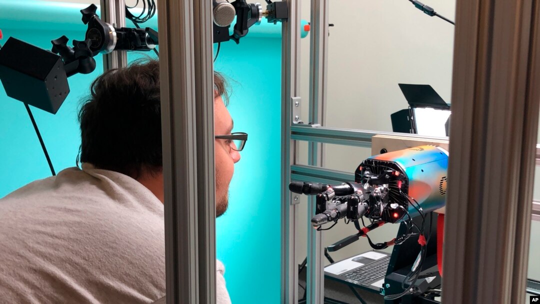 In this Thursday, July 26, 2018, photo, OpenAI researcher Jonas Schneider examines the research lab’s robotic hand in San Francisco. The hand, called Dactyl, has a single job, and that’s to rotate a cube until the letter facing up matches a random selection. (AP Photo/Ryan Nakashima)