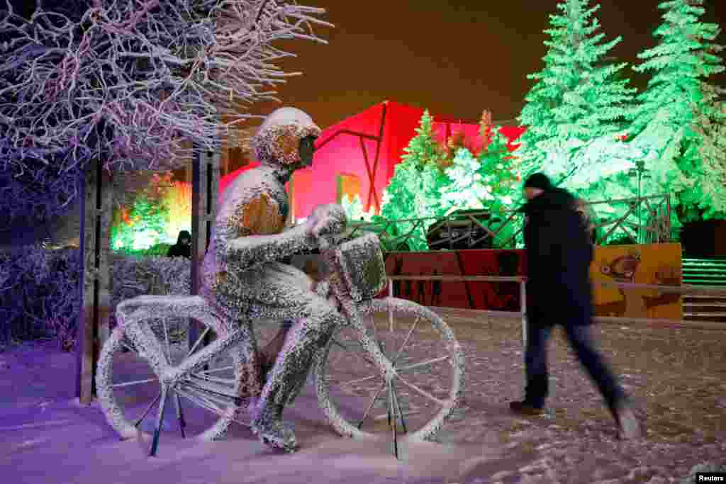 A man walks past a snow-covered installation depicting a bicyclist in Stavropol, Russia, Dec. 23, 2020.