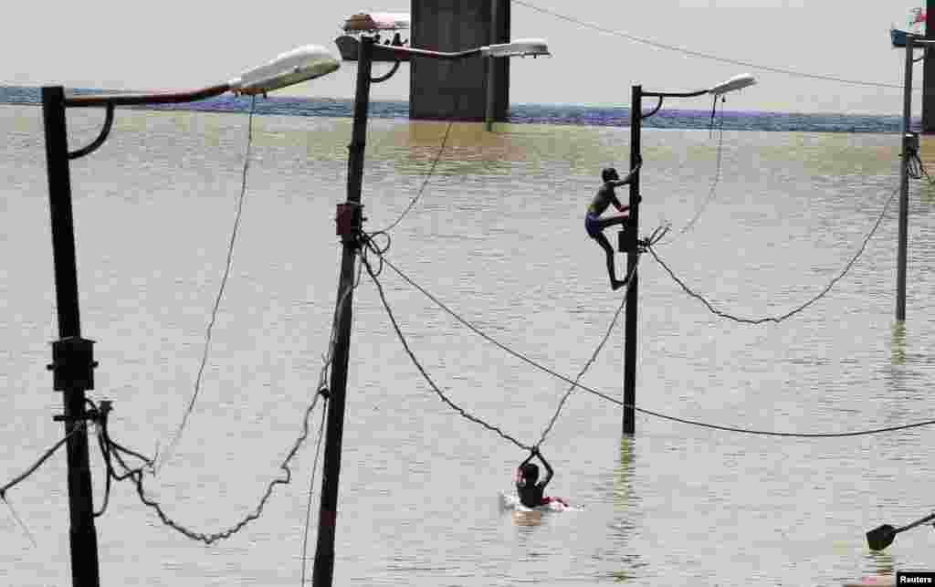 A boy climbs a partially submerged electric pole as he plays with others on the flooded banks of Ganga river, in Allahabad, India.