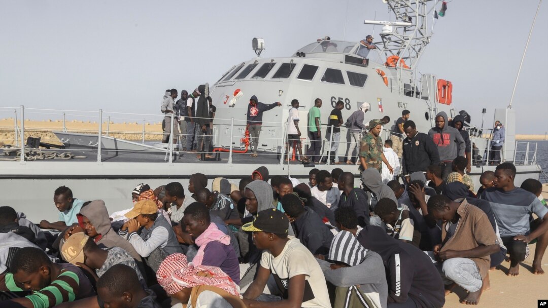 Rescued migrants are seated next to a coast guard boat in the city of Khoms, around 120 kilometers (75 miles) east of Tripoli, Libya, Tuesday, Oct. 1, 2019. (AP Photo/Hazem Ahmed)