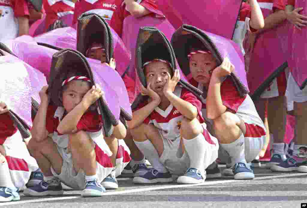 Anak-anak Taiwan menutupi kepala mereka dari sengatan matahari selama latihan untuk perayaan Hari Nasional di depan Kantor Kepresidenan di Taipei, Taiwan.
