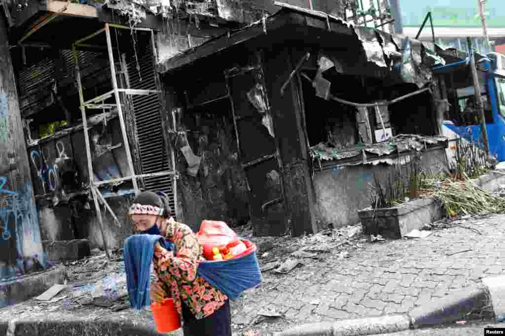 A traditional drink vendor reacts as she passes a burned police station a day after a protest against the government's jobs creation law which led to clashes between demonstrators and riot police near the Presidential Palace in Jakarta, Indonesia.