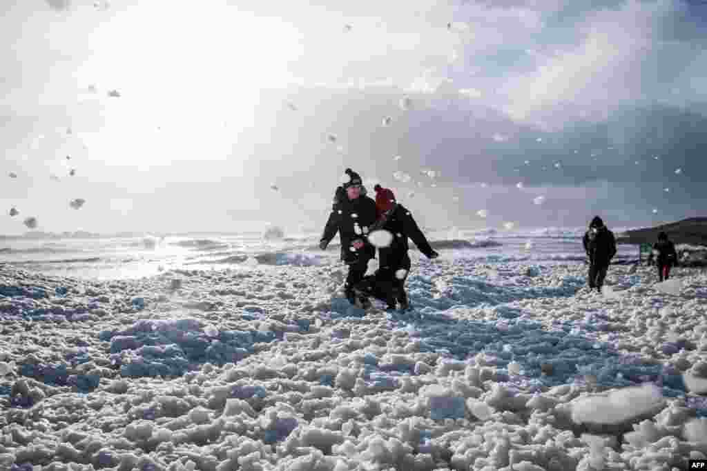 People walk in the foam in the La Torche beach in Plomeur, western France, as storm Bella caused torrential rain and heavy winds in much of the country.