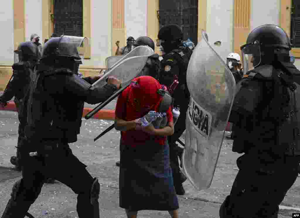 Riot police attack a demonstrator during a protest demanding the resignation of Guatemalan President Alejandro Giammattei, in Guatemala City, Nov. 21, 2020.