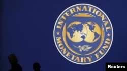 Visitors are silhouetted against the logo of the International Monetary Fund at the main venue for the IMF and World Bank annual meeting in Tokyo, October 10, 2012.