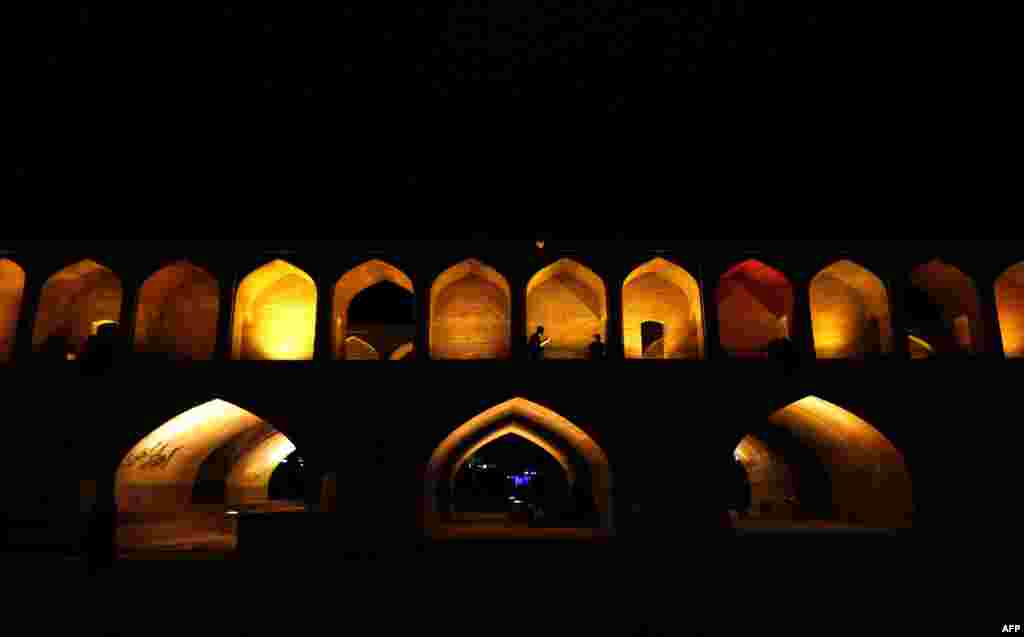 Iranians walk next to the "Si-o-Se Pol" bridge (33 Arches bridge) over the Zayandeh Rud river in Isfahan, which now runs dry due to water extraction before it reaches the city on April 12, 2018.