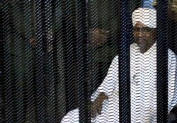 FILE - Sudan's former president Omar Hassan al-Bashir sits guarded inside a cage at the courthouse in Khartoum, Aug. 19, 2019.