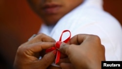 FILE - A red ribbon is put on the sleeves of a man by his friend to show support for people living with HIV during a program to raise awareness about AIDS on World AIDS Day in Kathmandu, Dec. 1, 2013. 
