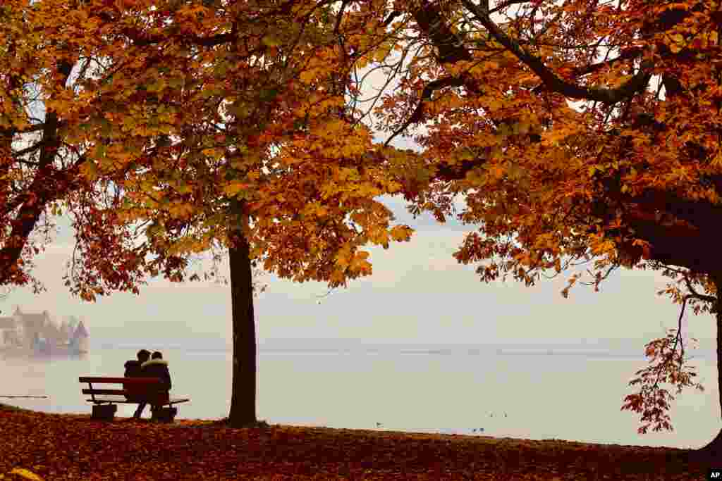 A young couple sits at the banks of Lake Constance on a misty fall day at Lotzbeck Park in Lindau, Germany.